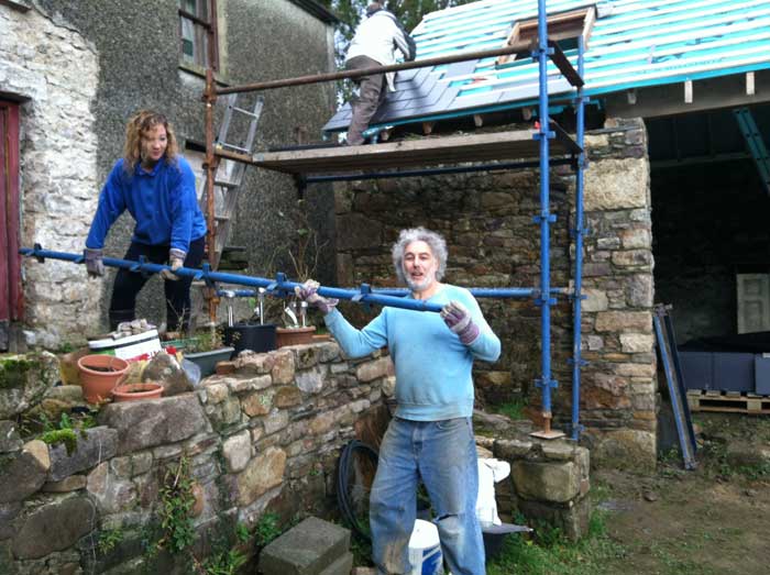 Allie handing Mike a big scaffold bar over the stone wall