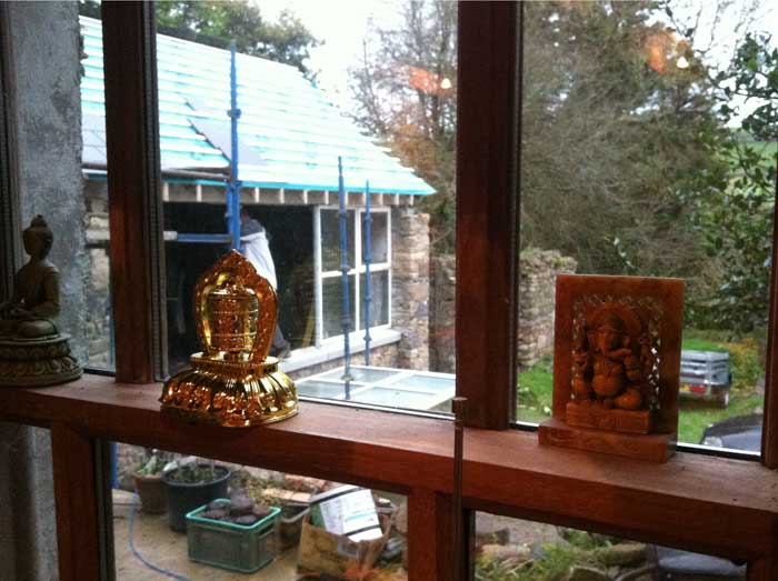 Green buddah, Tibetan prayer wheel and wooden Ganesh on the window ledge, with the new plastic-covered roof in the background