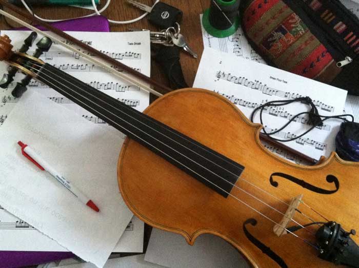 Violin on clutter of sheet music on laptop